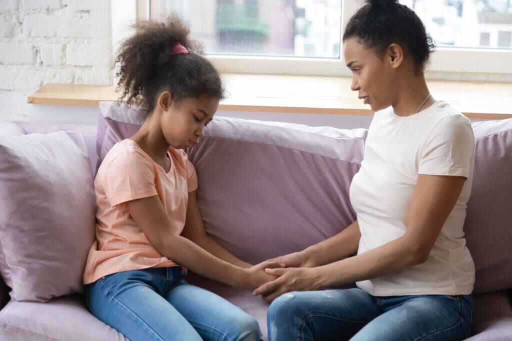 African mother school age daughter hold hands sit on couch having confidential conversation mom encourages supports little kid girl in her little problems or telling about separation with dad concept